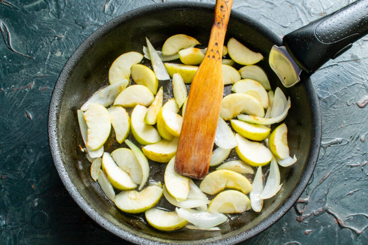 Sautéing onions and apples to build flavor. Sliced onions and apples being added to the skillet.