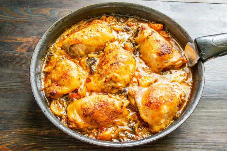 Basting the Chicken for Extra Flavor and Moisture Chicken thighs being basted with sauce from the pan while baking in the oven.