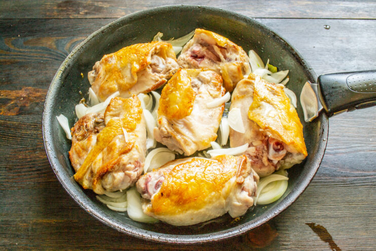Sautéing Onions with the Chicken Sliced white onion being added to the skillet with searing chicken thighs.