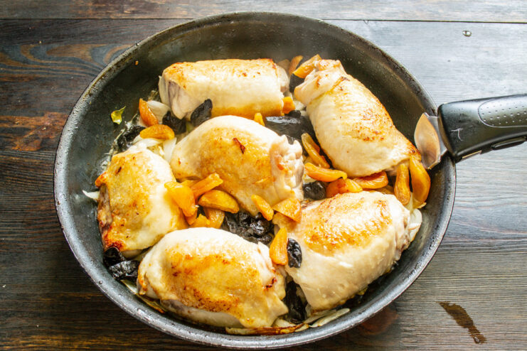 Adding Sweetness with Dried Fruits Chopped prunes and dried apricots being added to the chicken and onions in the skillet.