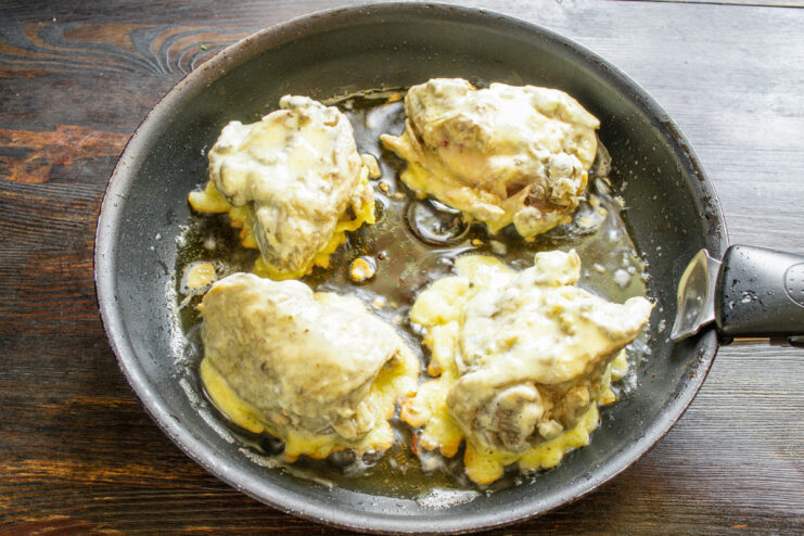 Battered chicken thighs sizzling in hot oil in a skillet.