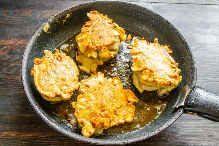 Using tongs to flip a golden-brown chicken thigh in a hot skillet.
