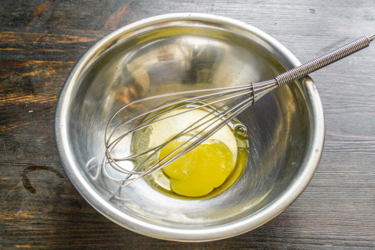 Two eggs being cracked into a white ceramic bowl.