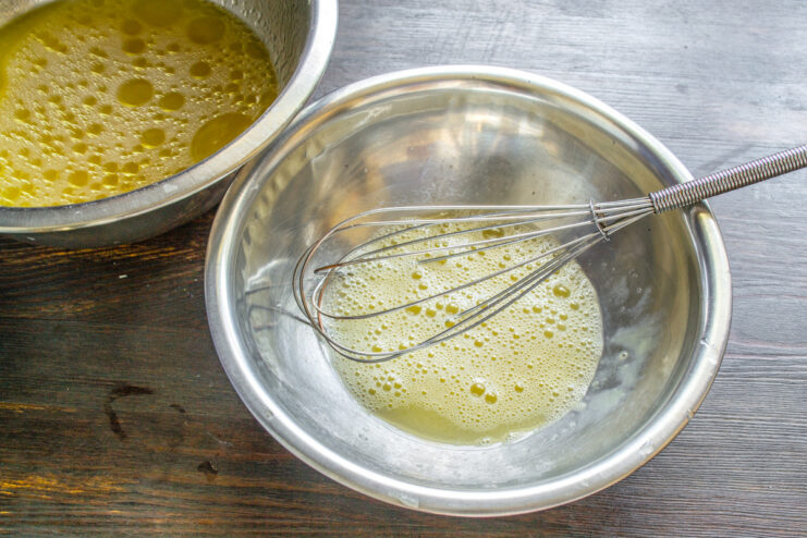 A metal whisk mixing eggs and salt in a white bowl.