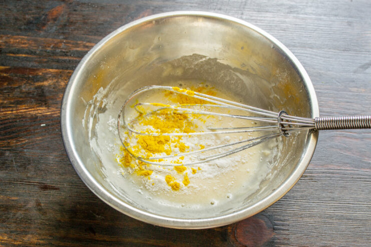 A spoonful of yellow ground turmeric being added to the batter mixture.