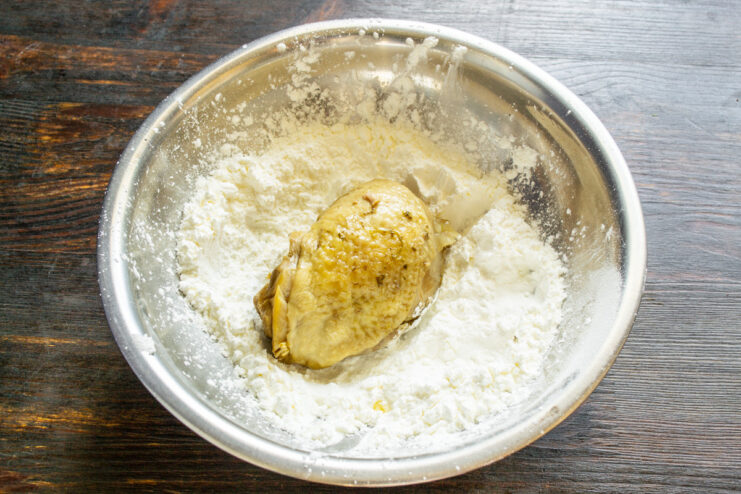 Four chicken thighs coated in starch resting on a wooden cutting board.