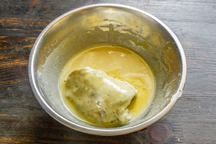 A chicken thigh being dipped into a bowl of yellow rice batter.