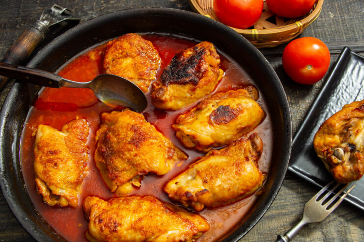 A dish of cooked chicken thighs in a rich red tomato sauce.