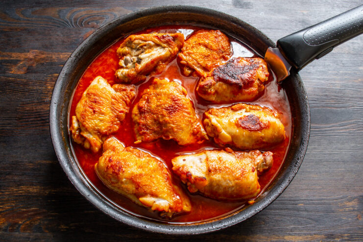 Transferring the Skillet to the Preheated Oven A skillet with chicken in bubbling tomato sauce, ready for the oven.