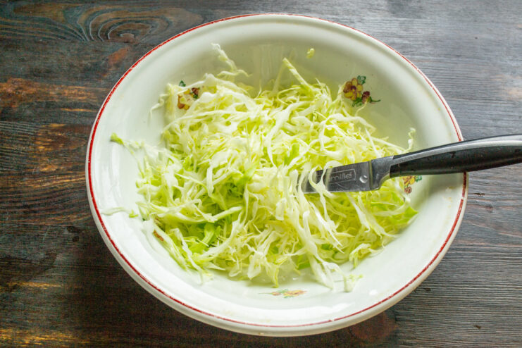 Preparing the cabbage for the chicken patties A pile of thinly shredded young cabbage in a clear glass bowl.