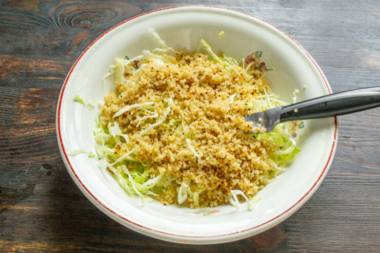 Adding cooked quinoa to the shredded cabbage Cooked quinoa being added to a bowl of shredded cabbage.