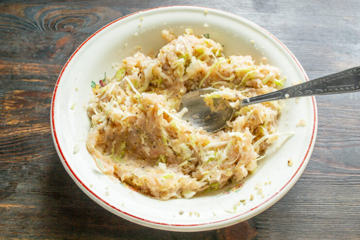 Mixing all the ingredients for the chicken patties A hand in a disposable glove mixing the ground chicken, quinoa, and cabbage in a bowl.