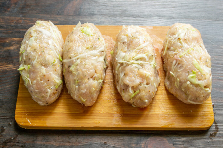Shaping the chicken and quinoa mixture into oval patties Four raw, oval-shaped chicken and quinoa patties on a wooden cutting board.