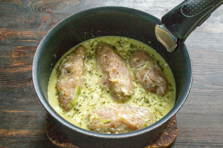 Placing the patties into the simmering sauce Raw chicken patties being placed into a saucepan with simmering yellow cream sauce.