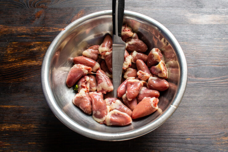 How to properly clean and prepare chicken hearts for cooking. Raw chicken hearts on a cutting board being trimmed of fat.