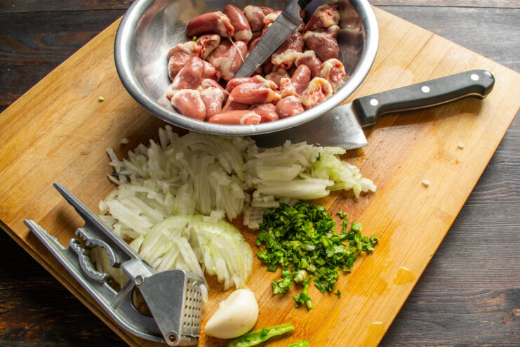 Finely chopping an onion is the first step for the aromatic base. A hand holding a knife, finely chopping a white onion on a cutting board.