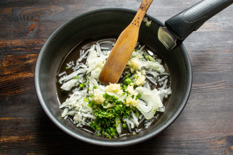 Sautéing onion, parsley, and garlic to build the flavor base for the sauce. Chopped onion, parsley, and garlic being sautéed in a hot skillet.