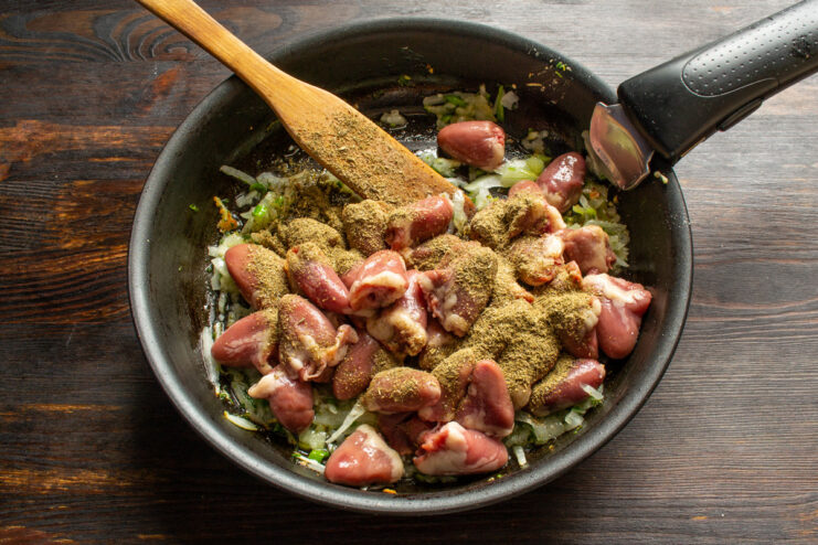 Adding Khmeli-Suneli, a fragrant Georgian spice blend, for authentic flavor. Sprinkling a blend of dried herbs and spices, khmeli-suneli, over chicken hearts in a skillet.