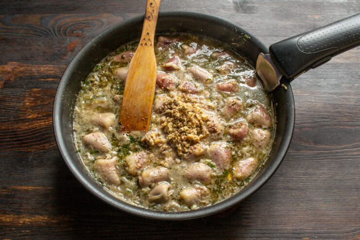 Adding ground walnuts to create the rich, creamy sauce. Adding a pile of ground walnuts to the chicken hearts stew in the skillet.