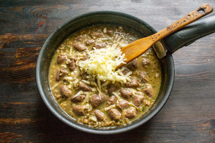Grated apple adds a subtle sweetness and tang to balance the rich sauce. Stirring grated apple into the chicken heart and walnut stew in a skillet.