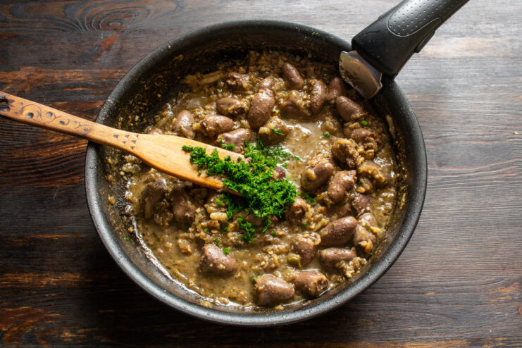 Finishing the dish with fresh dill for a burst of fresh flavor. Sprinkling freshly chopped dill over the chicken hearts stew in the skillet.