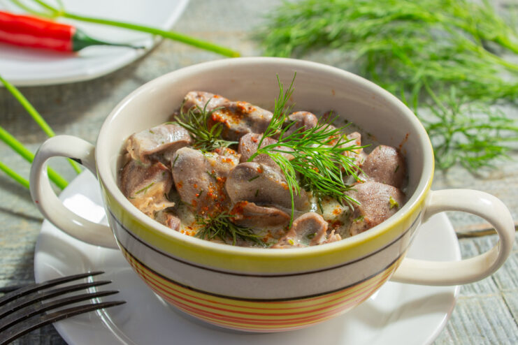 A bowl of cooked chicken hearts in a creamy white sauce, garnished with fresh dill.