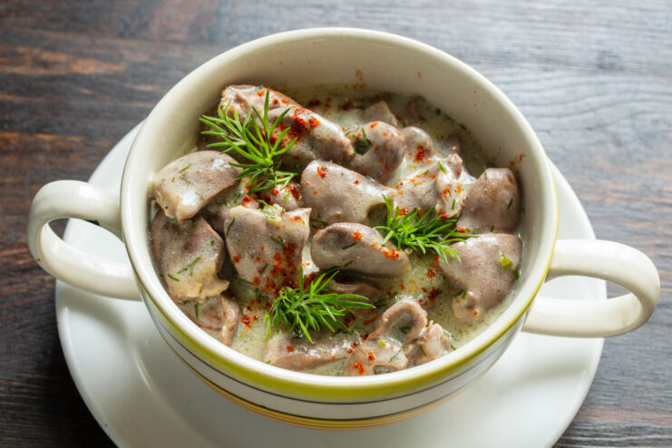 Serving the Chicken Hearts in Sour Cream Sauce Serving the finished chicken hearts in sour cream sauce from a pot into a white bowl.
