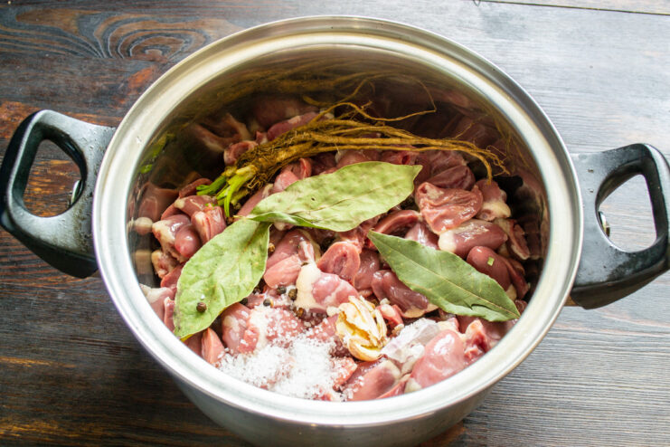 Step 2: Boiling the Hearts with Aromatics Raw chicken hearts in a pot with bay leaves, garlic, and parsley root before boiling.