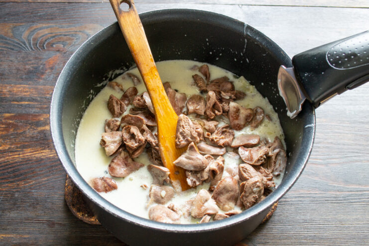 Step 6: Combining Hearts with the Sour Cream Sauce Adding cooked chicken hearts to the creamy white sauce in a pot.