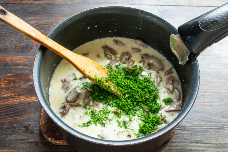 Step 7: Adding Fresh Dill and Garlic for Flavor Adding freshly chopped dill and minced garlic to the chicken hearts in cream sauce.