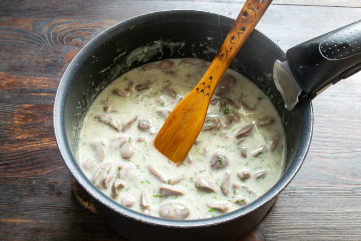 Step 8: Stirring to Combine All Ingredients Stirring the chicken hearts, dill, and garlic in the creamy sauce with a spatula.