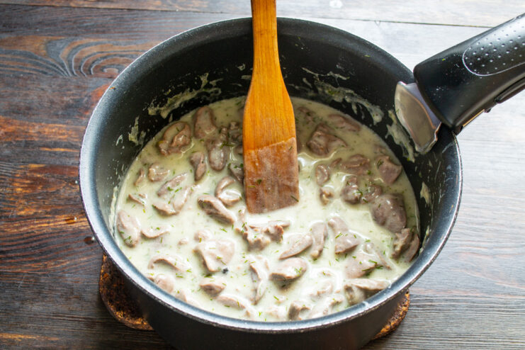 Step 9: Simmering the Dish to Thicken the Sauce Chicken hearts simmering gently in the sour cream sauce in a pot on the stove.