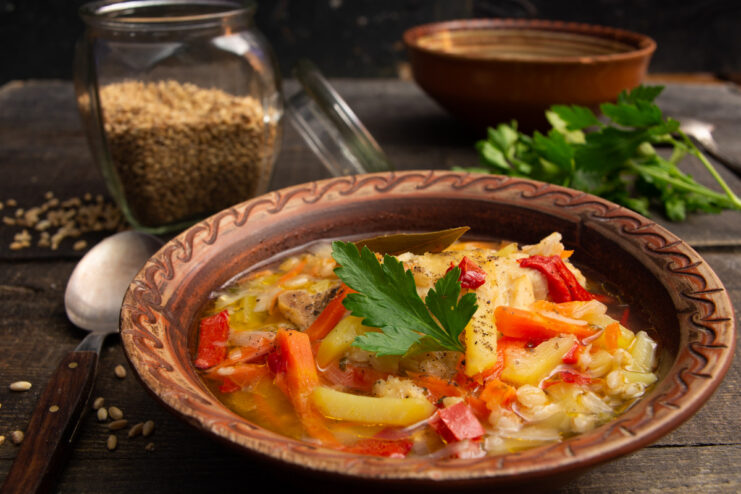 A bowl of ready-to-eat chicken soup with spelt and sweet pepper, garnished with herbs.