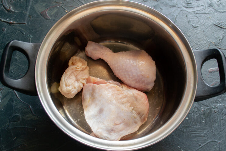 Step 1: Starting the chicken broth for the soup Raw chicken pieces placed in a large metal soup pot.