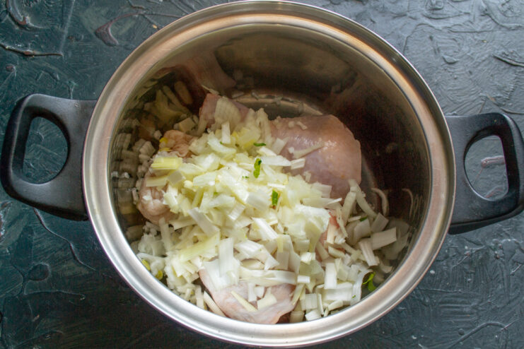 Adding aromatic leeks to the chicken for a flavorful base Chopped fresh leeks being added to the pot with raw chicken.