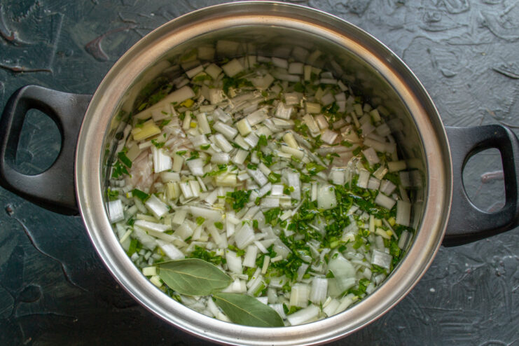 Adding water and salt to start cooking the soup A pot with chicken, leeks, and herbs being filled with water.