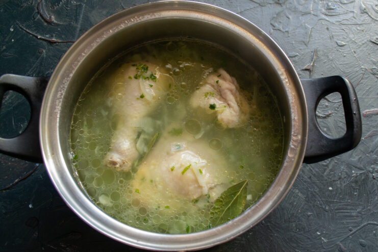Simmering the chicken broth to develop deep flavors Chicken soup simmering gently in a pot on the stove.