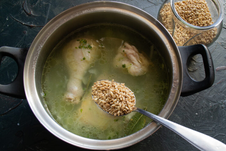 Adding nutritious spelt to the simmering chicken soup Dry spelt grains being poured into the simmering chicken soup.
