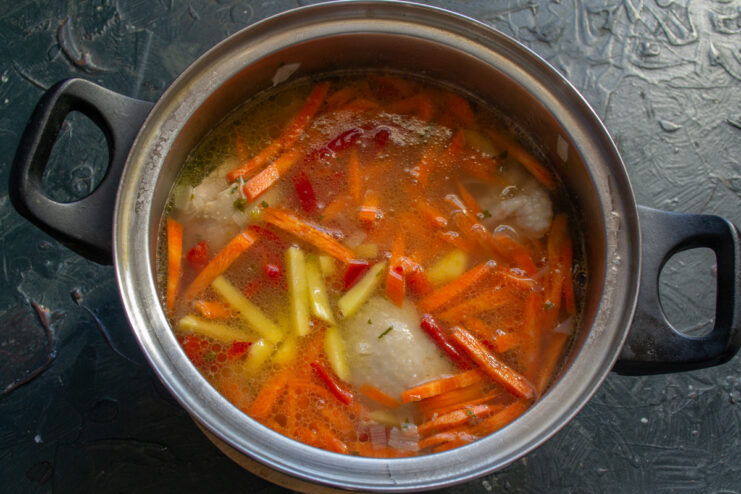 Adding the prepared vegetables to the soup pot A mix of chopped vegetables being added to the pot of chicken and spelt soup.
