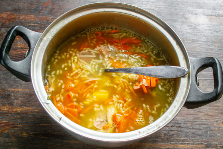 Simmering the Soup to Cook the Vegetables and Rice A pot of chicken soup simmering on the stove with a lid slightly ajar.