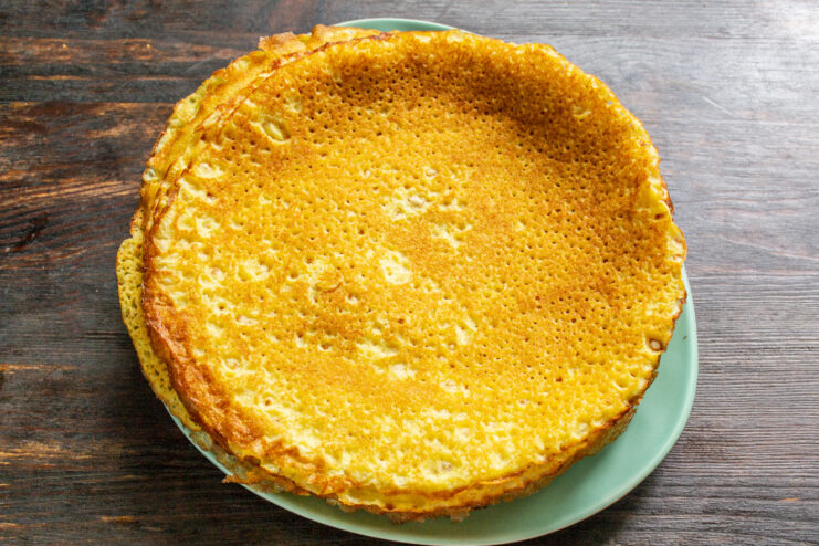 Frying Thin and Delicate Crepes for Lasagna A thin crepe being fried in a black skillet on a stovetop.