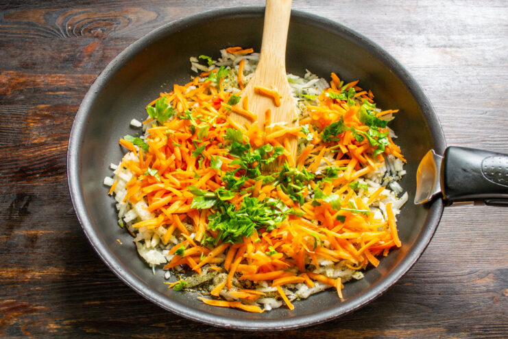 Adding Flavor with Carrots and Fresh Herbs Grated carrots and fresh parsley being added to sautéed onions in a pan.