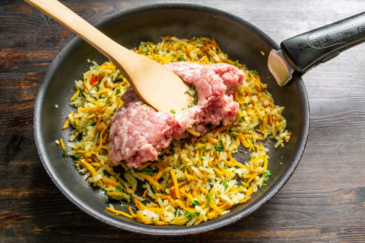 Browning the Ground Meat with Vegetables Ground meat being added to a pan with sautéed onions and carrots.