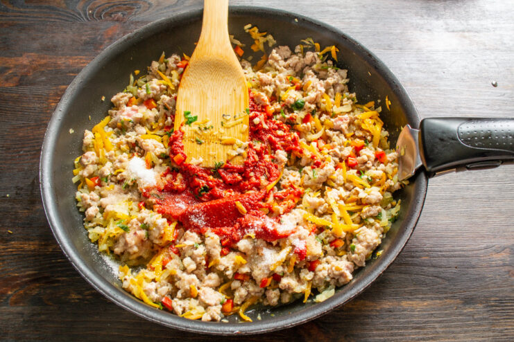 Creating a Rich Tomato Base for the Sauce Tomato paste being added to the ground meat sauce in a skillet.