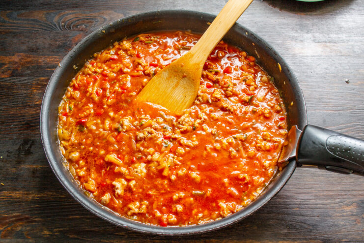 Simmering the Meat Sauce to Develop Flavors A rich meat sauce simmering in a deep skillet on the stove.