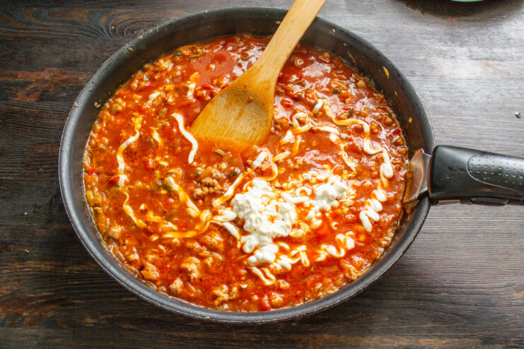 Adding Creaminess with Smetana or Heavy Cream Smetana (sour cream) being stirred into the meat sauce in a pan.