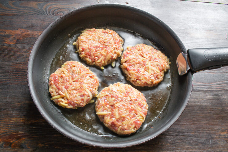 Frying the Kolduny to a Golden Brown Shaped kolduny patties being placed into a hot skillet with sizzling oil.