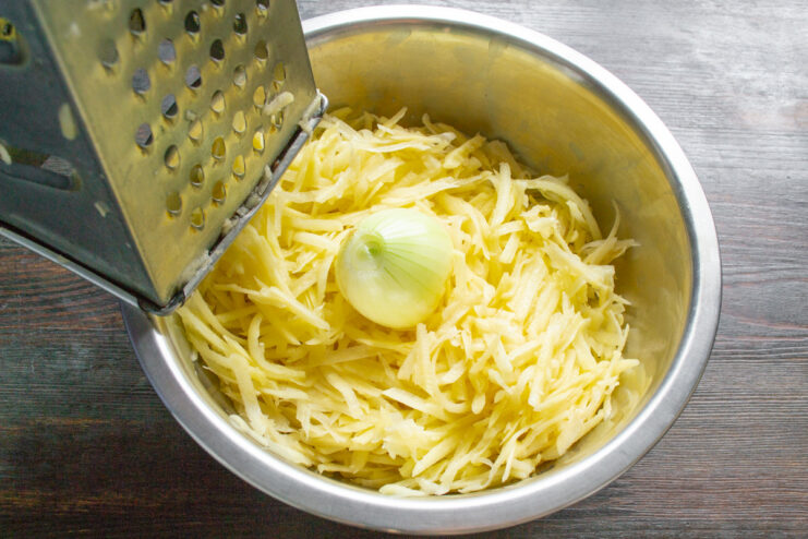 Adding Flavor: Combining Grated Onion with Potatoes Grated onion being added to a bowl of grated potatoes.