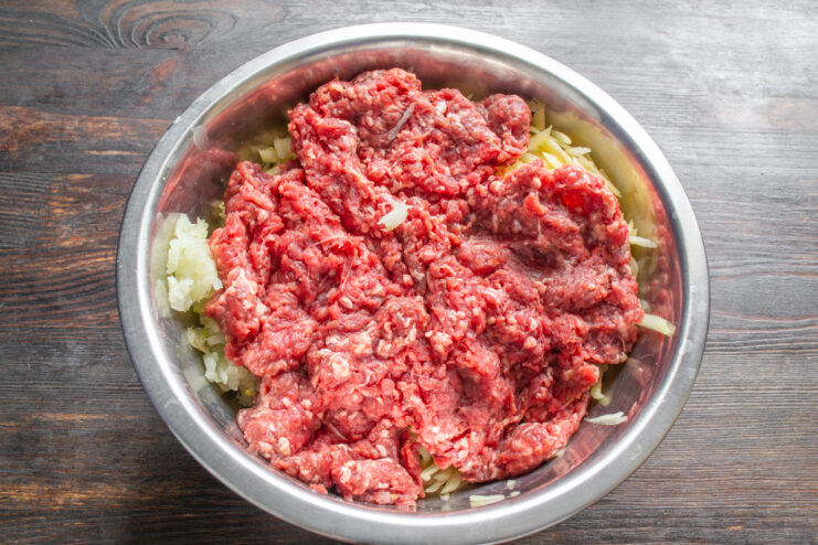 Preparing the Filling: Mixing in the Ground Beef A portion of chilled ground beef being added to the potato and onion mixture in a bowl.