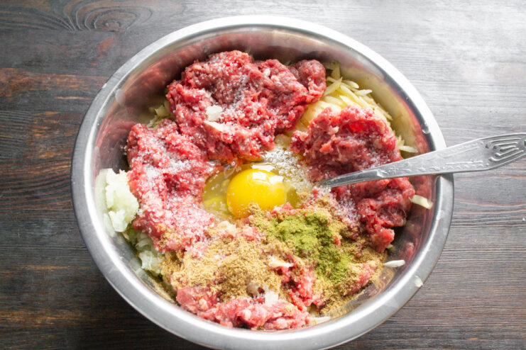 Seasoning the Kolduny Mixture for a Rich Flavor Spices being added to the potato and meat mixture in a glass bowl.